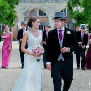 The bride and groom walk towards the camera whilst being followed by their bridesmaids and ushers along the main drive to the house