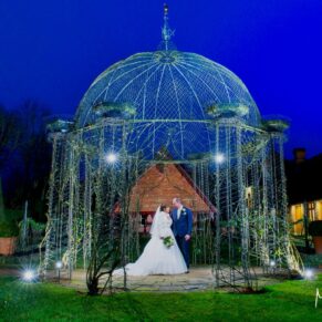 Buckinghamshire Winter Wedding Photography - the newlyweds framed by the floodlit rose arbour at The Dairy on the Waddesdon Estate