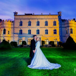Buckinghamshire Winter Wedding Photography - the newlyweds captured at dusk with the floodlit Hampden House behind them