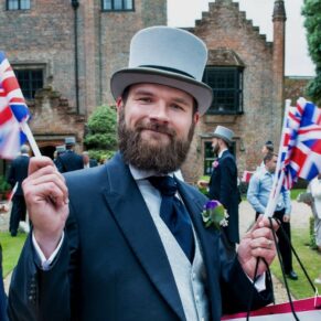Gentleman in top hat waving his wedding flags as the bride and groom arrive at the Chenies Manor reception from the church