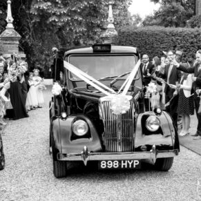 The newlyweds car arrives from the church through the middle of their cheering guests for their summer wedding at Chenies Manor