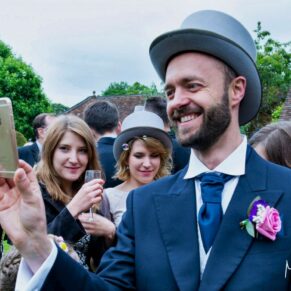 Reportage moment captured during the Chenies Manor drinks reception of one of the ushers taking a picture surrounded by some smiling wedding guests