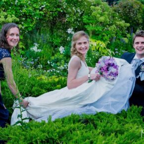 The bride is helped through the flower borders by two helpful friends at her Chenies Manor wedding