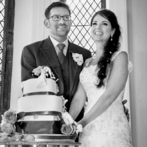 Photography of the wedding cake cutting captured in a huge feature window inside Clearwell Castle in the Forest of Dean