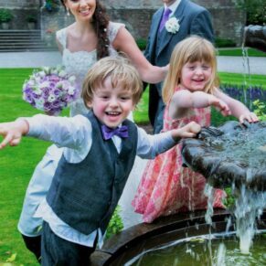 Kids larking around as they splash the photographer with water from the fountain during this summer wedding drinks reception at Clearwell Castle