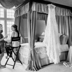 The wedding gown hangs on the four poster as the bride has her make-up done prior to her marriage ceremony at Clearwell Castle