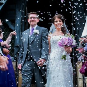 Colourful confetti aisle photography of the newlyweds at the parish church as they walk through their cheering guests before heading to their wedding reception at Clearwell Castle
