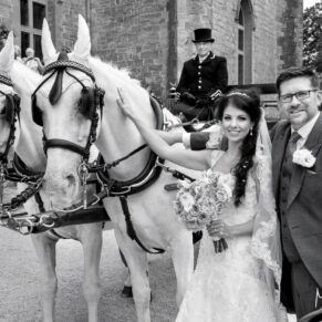Photography of the newlyweds posing with their gorgeous white horses and wedding carriage at the front of Clearwell Castle