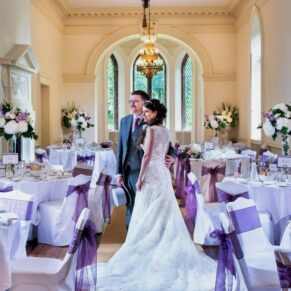 Photography of the bride and groom posing for a classic style wedding picture inside the dramatic dining room at Clearwell Castle
