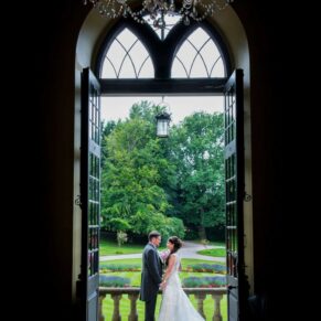 The newlyweds captured through the main doorway as they pose on the upper terrace steps at Clearwell Castle on their wedding day for a photography opportunity