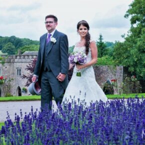 The happy couple walk between the lavender borders at their Clearwell Castle summer wedding