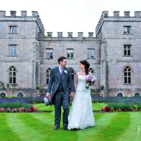 Photography of the smiling wedding couple walking straight towards the camera with Clearwell Castle and the extensive lavender borders behind them