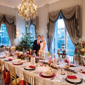 The couple pose beside their Christmas themed dining table in the Boudoir at their Cliveden House wedding