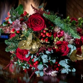 Stunning red Christmas wedding bouquet placed by the lit fireplace in the library at Cliveden House