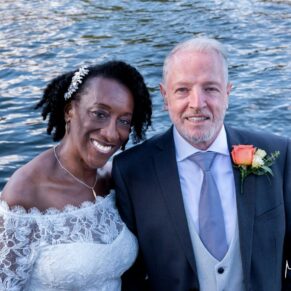 The joyous newlyweds pose for a close-up photo with the river behind them after their Compleat Angler wedding ceremony in Marlow