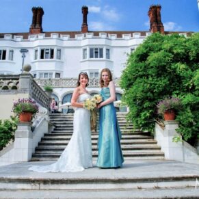 The bride with her bridesmaid on the garden steps under a perfect blue sky at this summer wedding celebration at Danesfield House Hotel