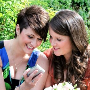 Two young ladies checking their phones during the wedding drinks reception at Danesfield House