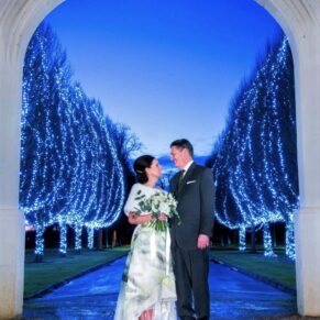 Night shot of the newlyweds under an archway with tree illuminations behind them at their Danesfield House winter wedding