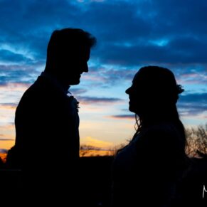 Close-up sunset silhouette pose of the newlyweds against a dramatic blue sky at their Farnham Castle wedding