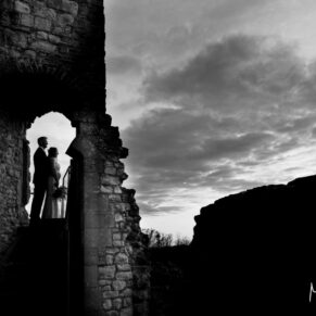 Silhouette pose of the bride and groom against a dramatic skyline captured through an archway at the summit of Farnham Castle