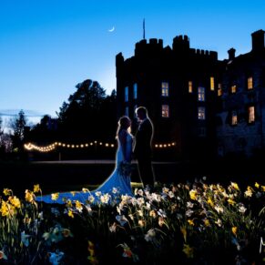 Silhouette floodlit shot of the bride and groom captured soon after dusk through the daffodil meadow at their Farnham Castle spring wedding
