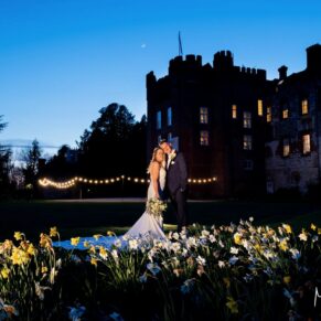 Floodlit shot of the bride and groom captured through the daffodils at their spring wedding at Farnham Castle