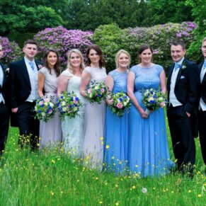 The bridal party pose for a group shot in the colourful wild flower meadow next to the church on the estate