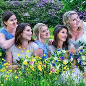 The bride with her bridesmaids sat in the colourful summer wild flower meadow