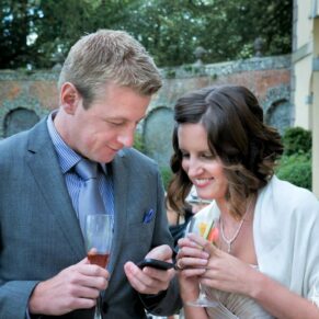 Guests enjoying the drinks reception in the gardens whilst checking out the photos they've taken on their phones