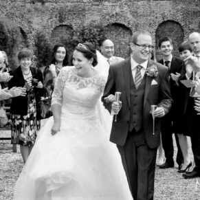 Action shot of the newlyweds walking through their confetti aisle whilst being cheered on by their lively guests