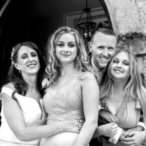 The newlyweds in a doorway with their bridesmaids enjoy a group hug