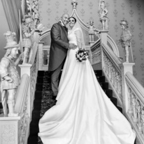 The newlyweds captured in a formal pose on the grand staircase during their wedding day celebrations at Hartwell House