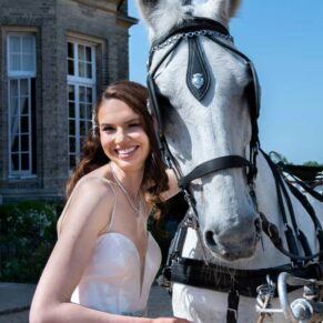The bride poses with her horse outside the main historic house after her carriage ride to the venue for her wedding reception
