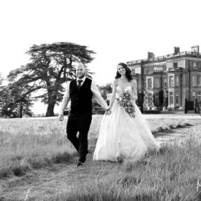 The newlyweds take a stroll in the grassy meadow of Hedsor House with the wedding venue behind them