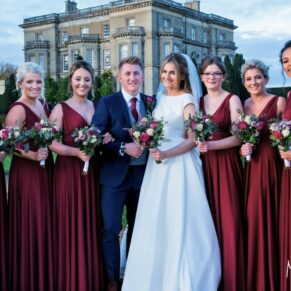 The newlyweds with their bridesmaids captured looking at the camera with Hedsor House in the distance