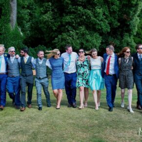Photography of a group of smiling wedding guests walking arm in arm through the gardens of the Latimer Estate