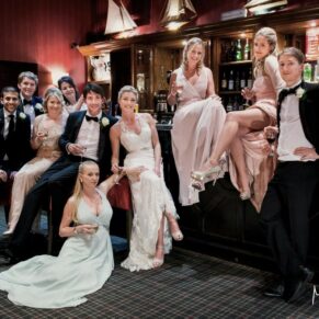 The newlyweds strike a fun group photography pose in the bar area with the bridal party during their Latimer Estate evening wedding reception