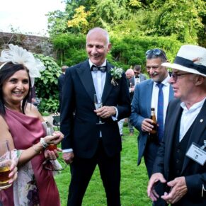 Reportage shot of some guests giggling along with the magician during the summer drinks reception in the gardens