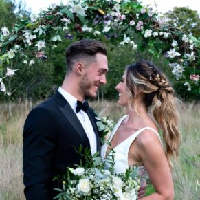 The bride and groom gaze at one another in the outdoor flower arch at their Old Windsor marriage