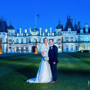 The newly married couple in front of the floodlit Waddesdon Manor at dusk with gorgeous dusky blue skies above