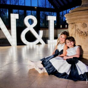 Two cute flower girls captured sat on the dancefloor with giant illuminated letters behind them at this wedding reception at The Dairy