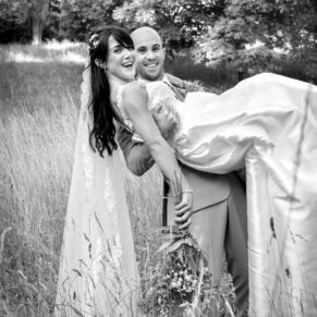 The groom lifts his wife to carry her through a meadow on the Waddesdon Estate