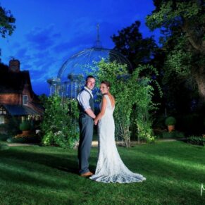 Dramatic floodlit pose of the newlyweds by the rose arbour at dusk on their wedding day at The Dairy on the Waddesdon Estate