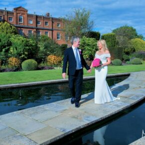 The bride and groom take a stroll beside the waters edge at their Grove Hotel summer wedding reception in Watford