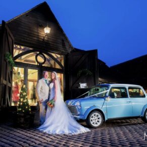 Old Luxters Wedding Photography - the newlyweds pose with their vintage mini at dusk outside the barn