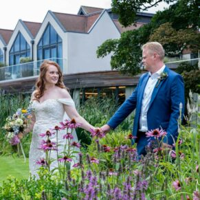 The bride and groom walk amongst the colourful flower borders at their Swan at Streatley wedding reception