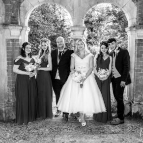 Black and white group pose of the bridal party in the folly at the Tudor Barn