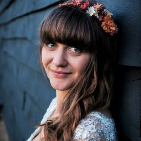 The bride poses for the camera stood against a dark wooden backdrop outside the venue