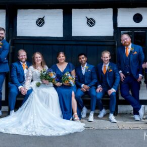 The wedding party casually pose for the camera on an old bench at the front of the historic Olde Bell Hotel in Hurley