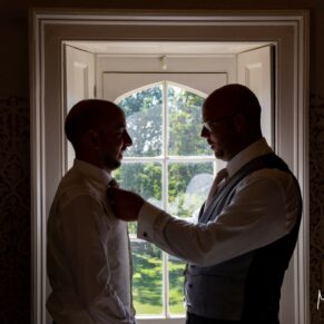 Silhouette shot of the groom and best man adjusting their ties before the ceremony at Weston Manor Hotel
